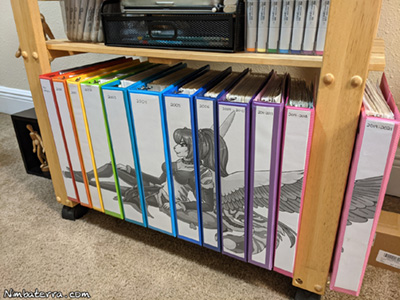 A bookshelf with art supplies sitting on the top shelf, with a picture of Tacoma the Tiger spanning across the binders of several books. Tacoma wears her hair up in a ponytail, her stripes clearly visible as she declines, and her giant fluffy tail behind her.